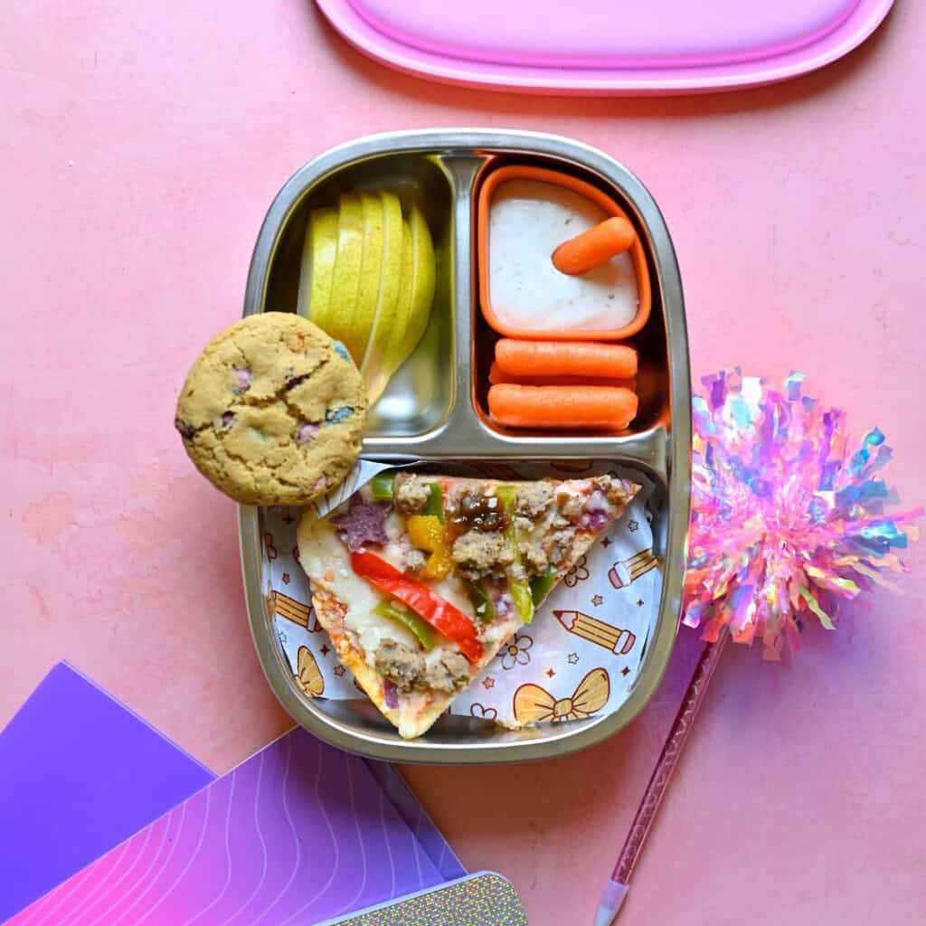 Back-to-school leftovers lunch with cold pizza, baby carrots and ranch, sliced pear and a cookie.