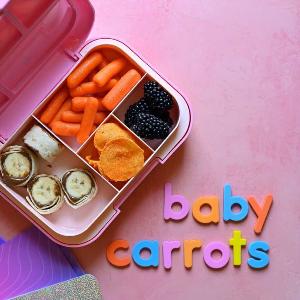 Snack-style school lunch with banana sunflower butter roll-ups, baby carrots, buffalo chicken chips and blackberries.