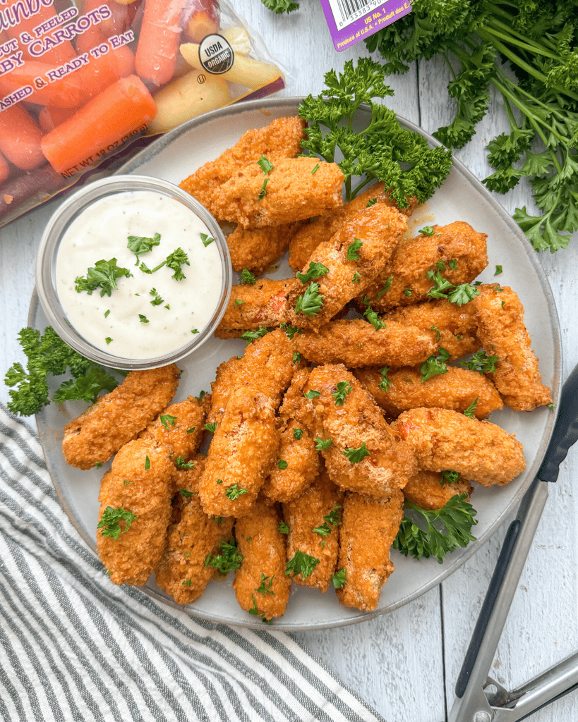 Buffalo baked baby carrots garnished with parsley, served on a platter with creamy dipping sauce.