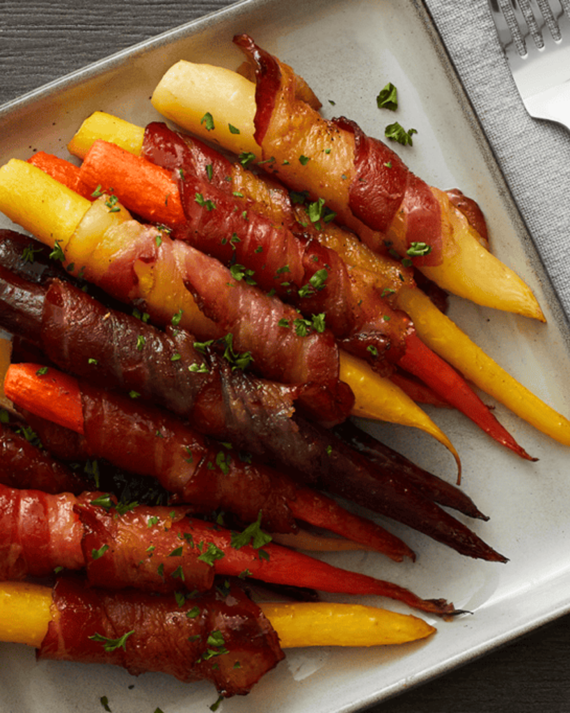 Maple bacon-wrapped rainbow carrots garnished with chopped herbs on a rectangular platter.